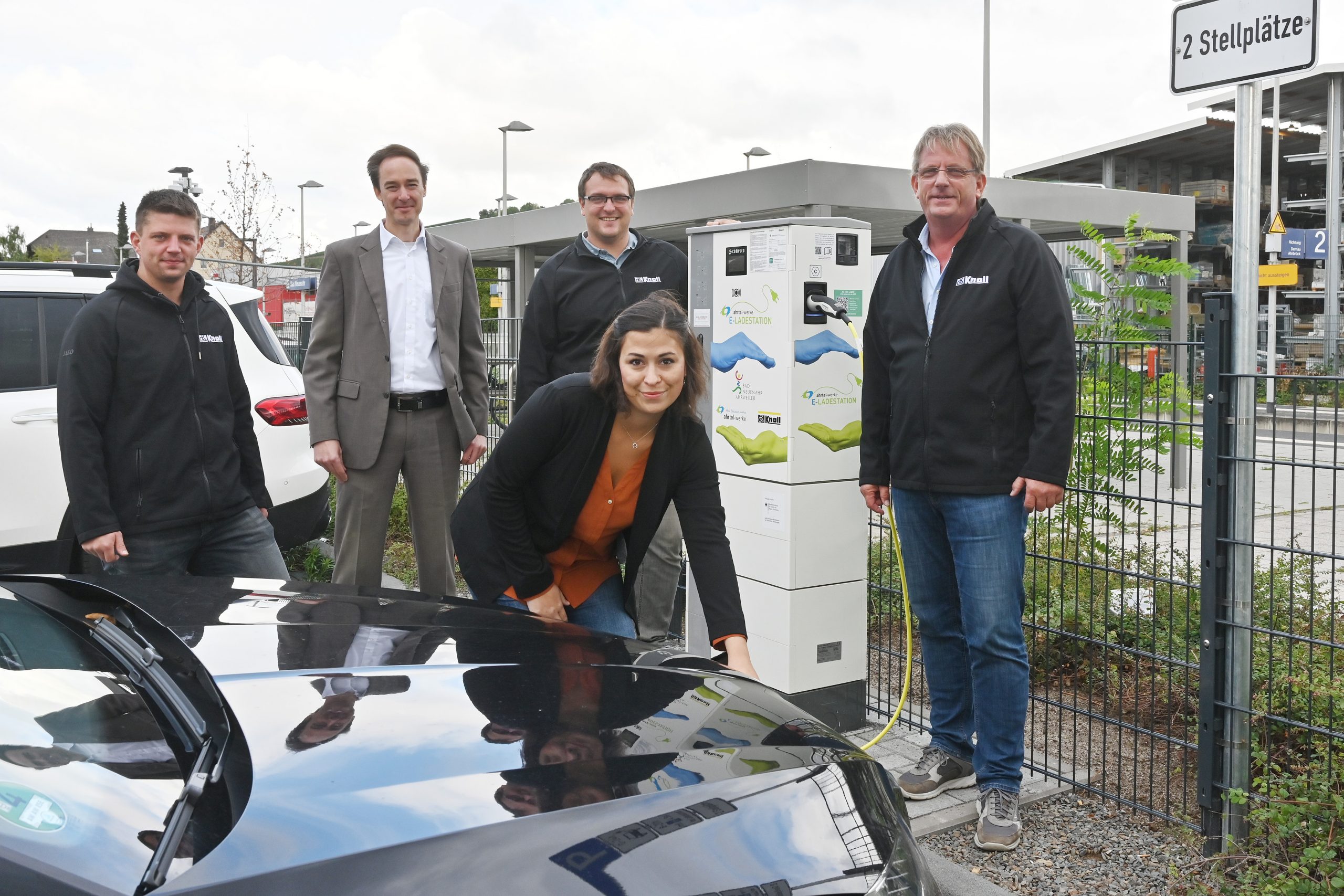 Foto: Die Herren Daniel Wassong (Knoll GmbH & Co. KG), Dominik Neswadba (Ahrtal-Werke), Robert Helmrich (Knoll GmbH & Co. KG) und Dirk Wassong (Knoll GmbH & Co. KG) weihen gemeinsam mit Lydia Papadopoulos im Vordergrund (Stadt Bad Neuenahr-Ahrweiler) die neue Ladesäule am Bahnhof von Bad Neuenahr ein 
